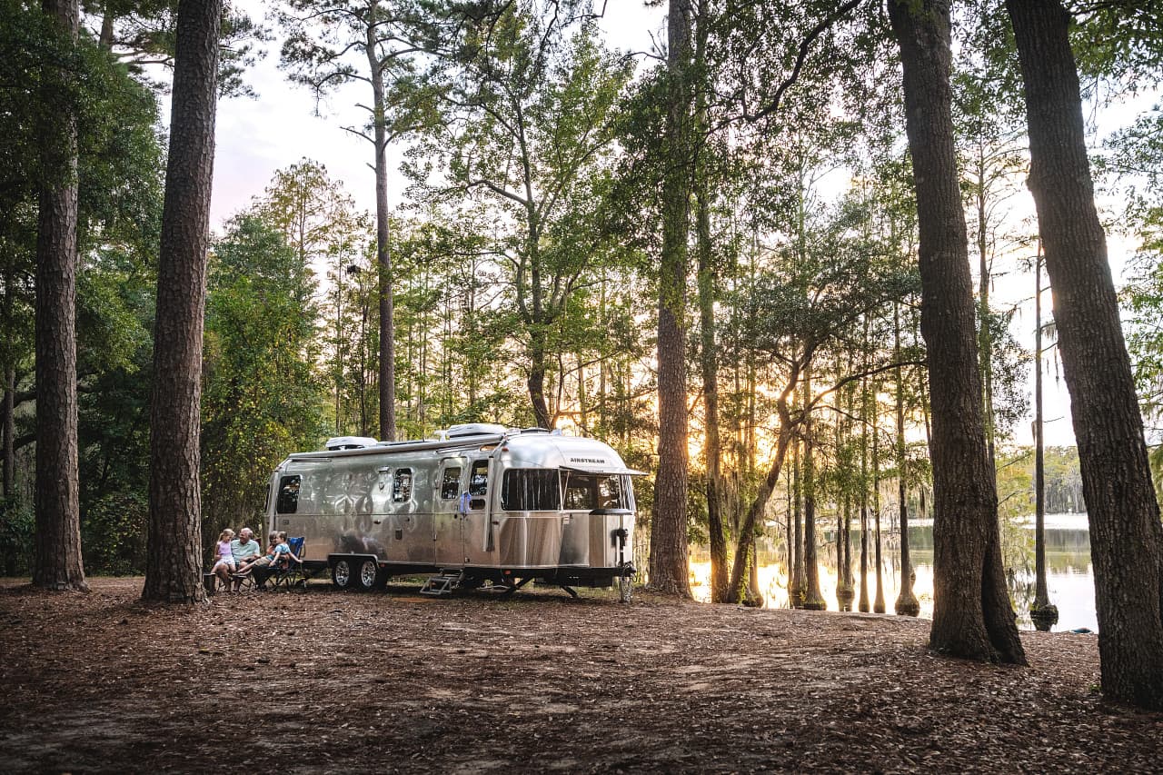 Airstream Classic travel trailer beside a lake in a wooded campground